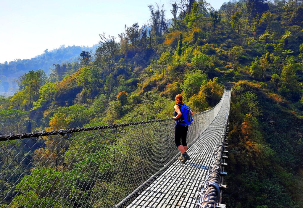 Trekkerin über eine Hängebrücke in Nepal, in der Annapurna Region