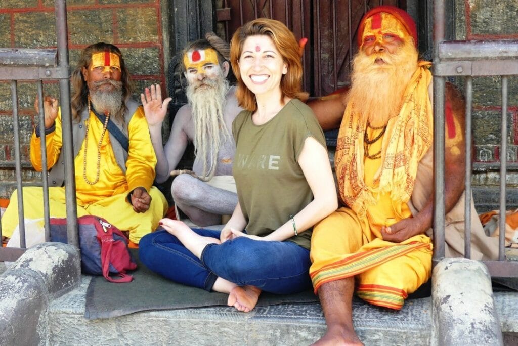 Frau sitzt in Yoga Position mit 3 heiligen Männern, die bunt bemalt sind